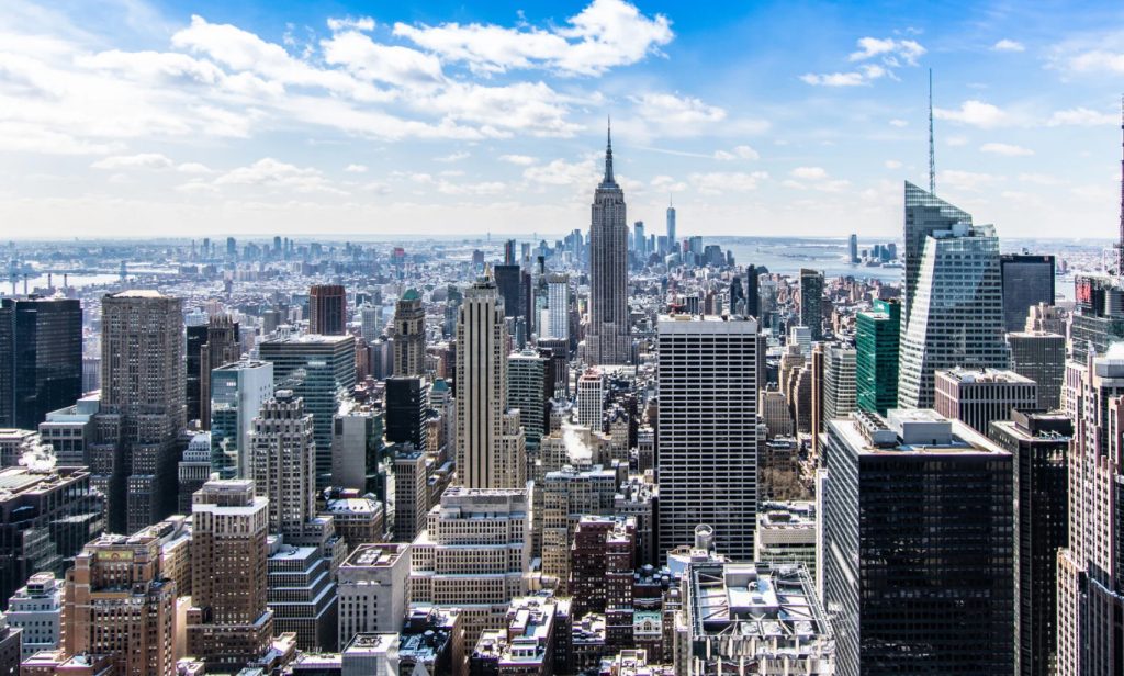 A wide view of a city skyline with many tall skyscrapers under a blue sky with scattered clouds.
