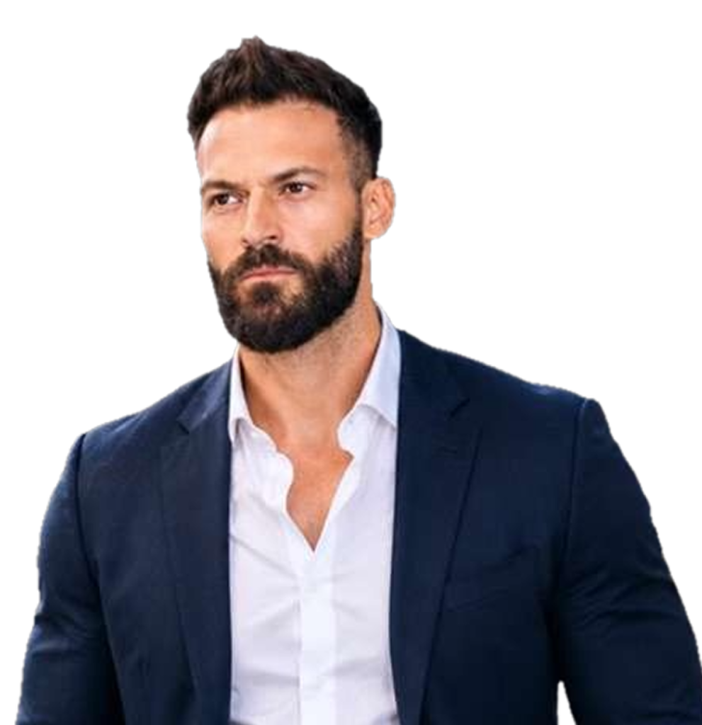 A man with short dark hair and a beard wears a navy blue suit jacket over a white shirt, standing against a plain white background.