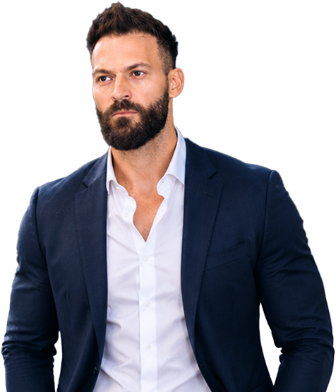 A man with dark hair and a beard wears a navy suit jacket over a white shirt. He stands against a plain light background, looking slightly to the side with a serious expression.